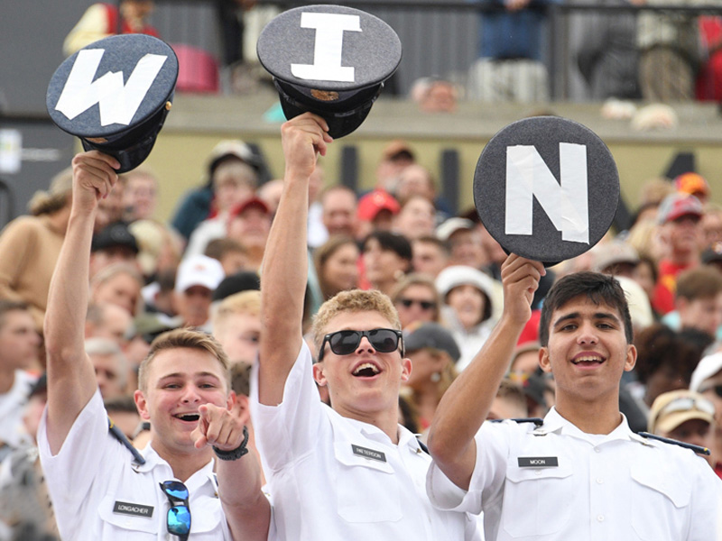 ֻ̳cadets in stands cheer a sports team and hold up hats that spell out W I N